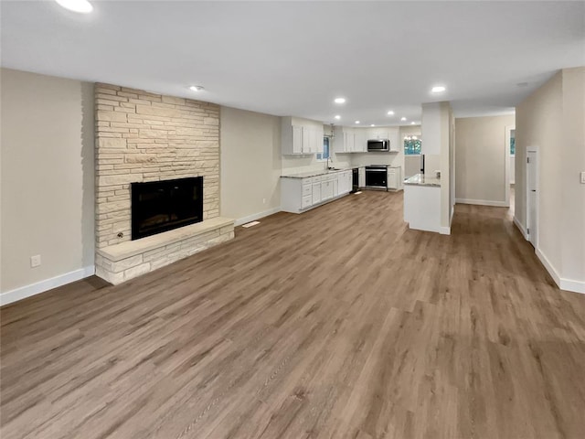 unfurnished living room featuring a stone fireplace, sink, and light wood-type flooring