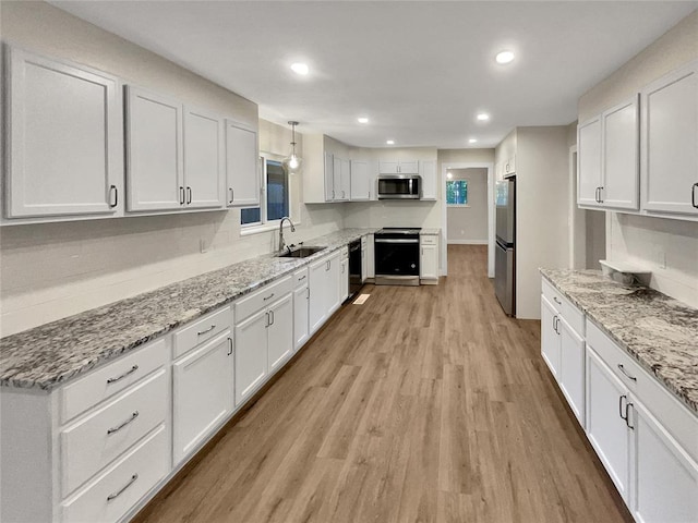 kitchen with appliances with stainless steel finishes, light wood-type flooring, sink, white cabinetry, and hanging light fixtures