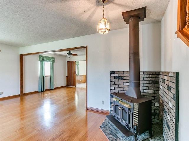 unfurnished living room with a textured ceiling, light hardwood / wood-style floors, a wood stove, and ceiling fan