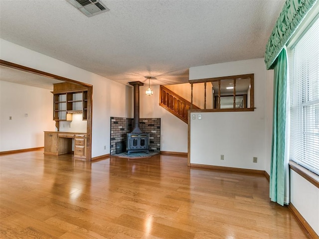 unfurnished living room featuring a textured ceiling, light wood-type flooring, a wood stove, and built in desk