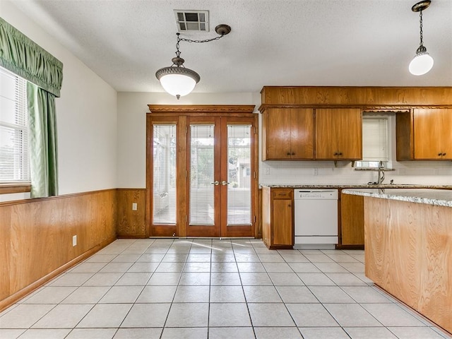 kitchen featuring french doors, wooden walls, dishwasher, and decorative light fixtures