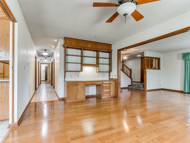 unfurnished living room featuring a textured ceiling, built in desk, light hardwood / wood-style floors, and ceiling fan