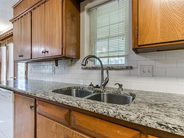 kitchen featuring decorative backsplash, dishwasher, sink, and light stone countertops