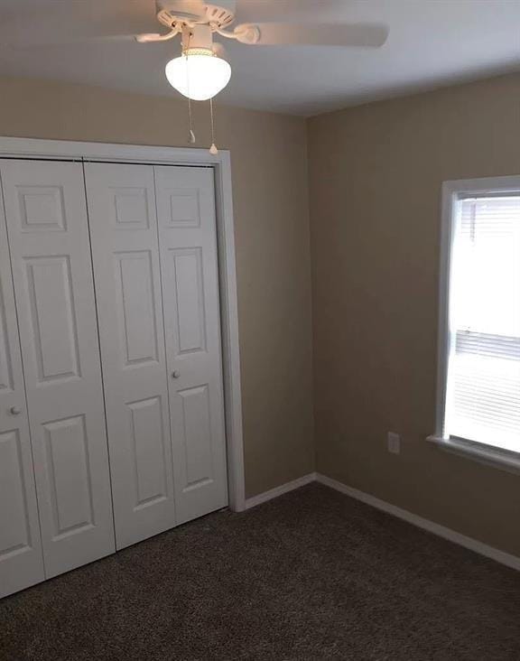 unfurnished bedroom with dark colored carpet, ceiling fan, and a closet