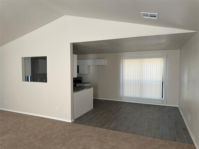 unfurnished living room with vaulted ceiling and dark colored carpet