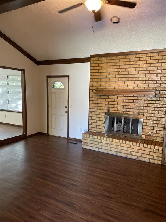 unfurnished living room with a brick fireplace, dark hardwood / wood-style floors, a textured ceiling, lofted ceiling, and ornamental molding