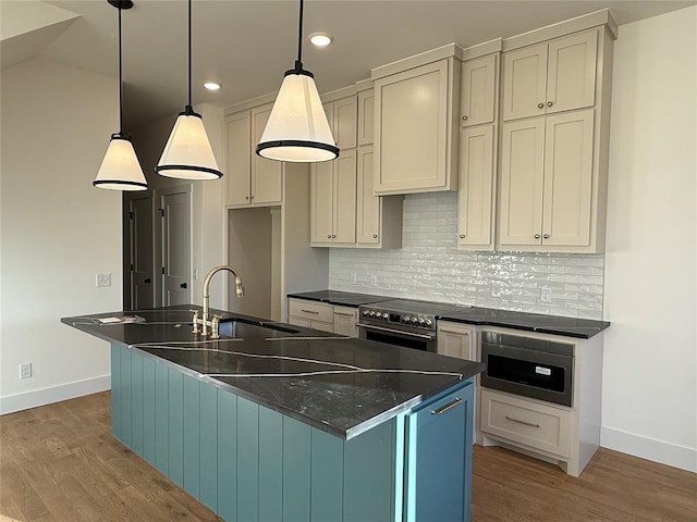 kitchen featuring an island with sink, light wood-style flooring, appliances with stainless steel finishes, hanging light fixtures, and backsplash