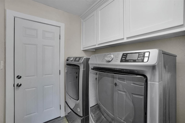 laundry room with hardwood / wood-style flooring, cabinets, and washing machine and dryer