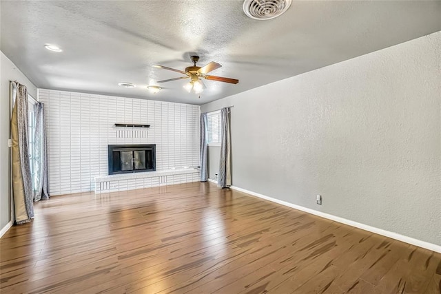 unfurnished living room featuring ceiling fan, a fireplace, wood-type flooring, and a textured ceiling