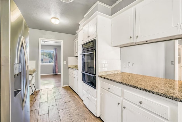 kitchen featuring white cabinets, light hardwood / wood-style flooring, stainless steel fridge, dark stone countertops, and a textured ceiling