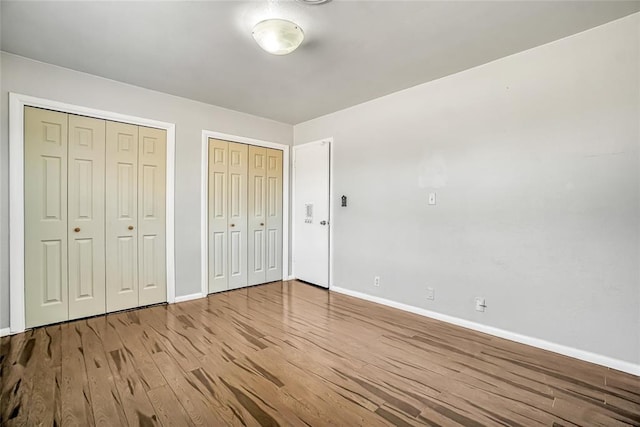 unfurnished bedroom with hardwood / wood-style floors and two closets