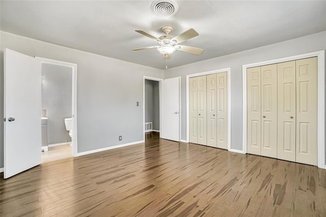 unfurnished bedroom with ceiling fan, light wood-type flooring, connected bathroom, and multiple closets