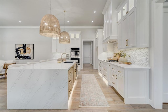 kitchen with white cabinets, hanging light fixtures, light hardwood / wood-style flooring, decorative backsplash, and a large island