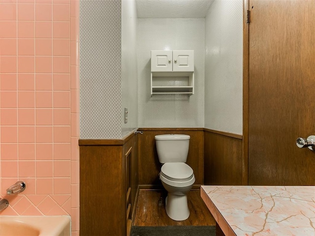 bathroom with a washtub, hardwood / wood-style floors, toilet, and wood walls