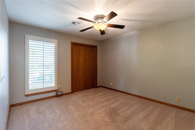 unfurnished bedroom featuring light carpet, a textured ceiling, a closet, and ceiling fan