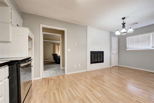 unfurnished living room featuring a fireplace, light hardwood / wood-style floors, a textured ceiling, and a notable chandelier