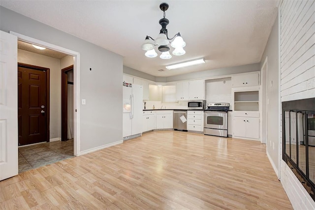 kitchen featuring appliances with stainless steel finishes, decorative light fixtures, white cabinetry, and light hardwood / wood-style floors