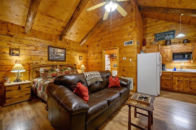 bedroom featuring wood walls, white fridge, wood-type flooring, and beam ceiling