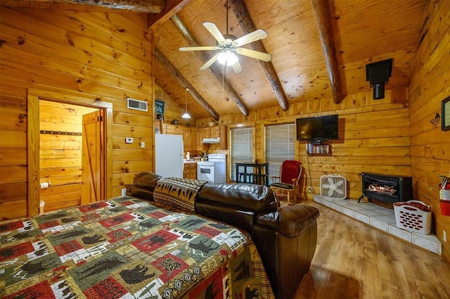 bedroom featuring a wood stove, vaulted ceiling with beams, white refrigerator, wooden walls, and light wood-type flooring