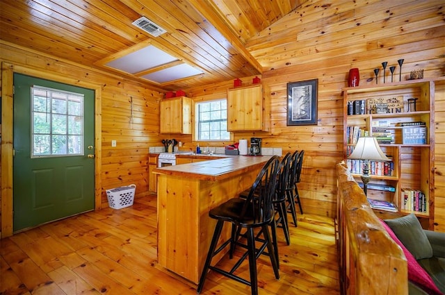 kitchen featuring a kitchen breakfast bar, vaulted ceiling, light brown cabinets, light hardwood / wood-style floors, and tile counters