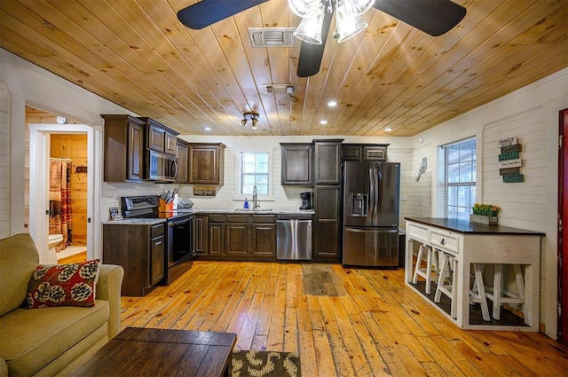 kitchen with wooden walls, light hardwood / wood-style flooring, stainless steel appliances, and dark brown cabinets