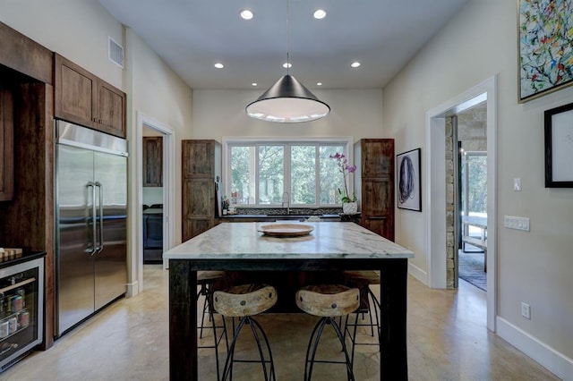 kitchen featuring light stone countertops, a center island, built in refrigerator, wine cooler, and hanging light fixtures