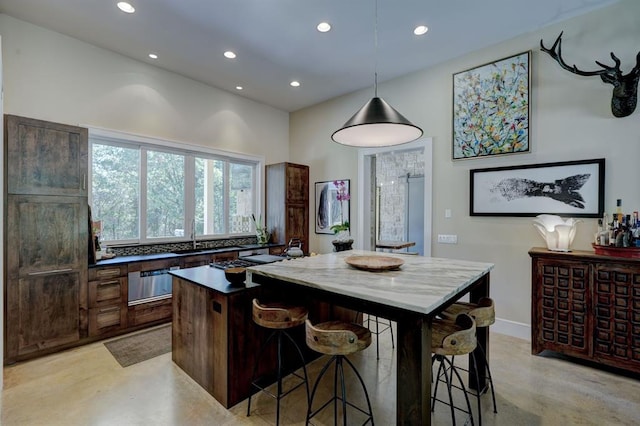 kitchen with dark brown cabinetry, hanging light fixtures, stainless steel gas cooktop, a breakfast bar, and a kitchen island