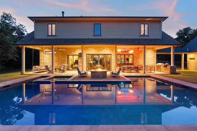 back house at dusk featuring ceiling fan, exterior kitchen, a fire pit, and a patio