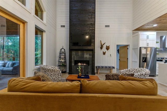 living room featuring a fireplace, wood-type flooring, a towering ceiling, and wood walls