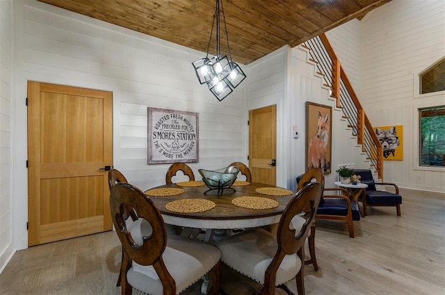 dining room with a high ceiling, wooden walls, light hardwood / wood-style flooring, a notable chandelier, and wood ceiling