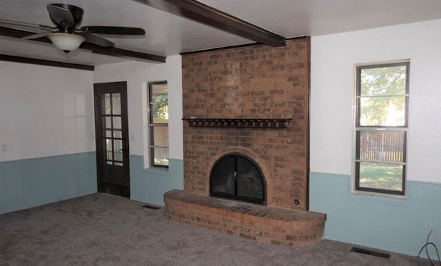 unfurnished living room featuring beamed ceiling, plenty of natural light, ceiling fan, and carpet