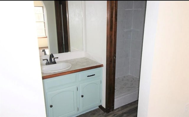 bathroom with a tile shower, vanity, and wood-type flooring