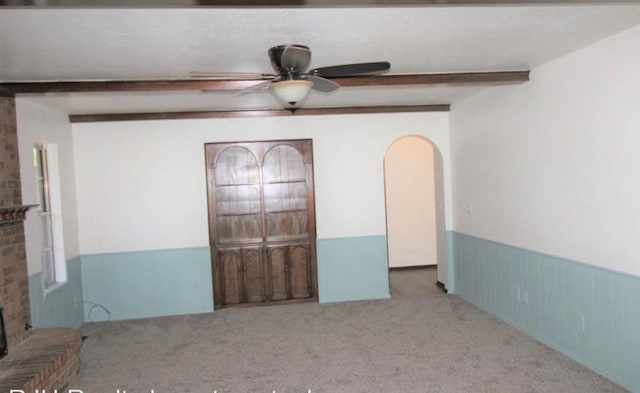 unfurnished bedroom with carpet, a brick fireplace, ceiling fan, wooden walls, and beam ceiling