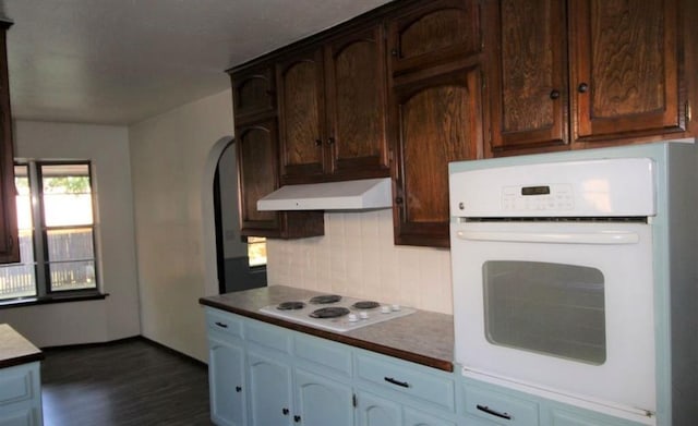 kitchen featuring decorative backsplash, white appliances, dark brown cabinetry, and dark wood-type flooring