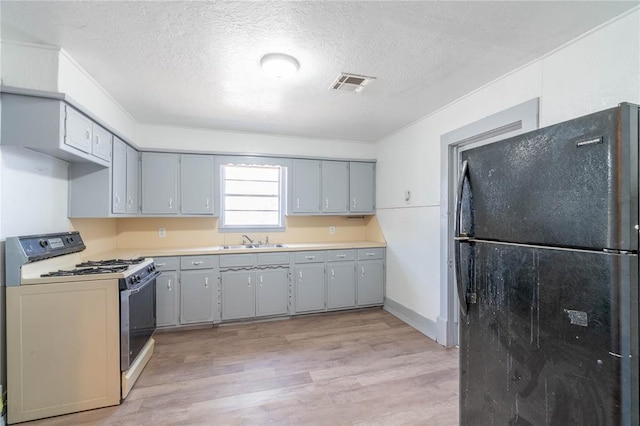 kitchen featuring light wood-type flooring, black fridge, a textured ceiling, sink, and white stove