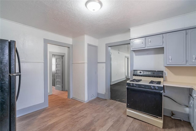 kitchen featuring black refrigerator, gray cabinets, white range with gas cooktop, and light hardwood / wood-style floors