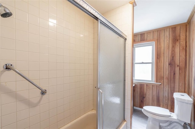 bathroom featuring bath / shower combo with glass door, toilet, and wood walls