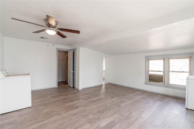 empty room with ceiling fan, independent washer and dryer, a textured ceiling, and light hardwood / wood-style flooring