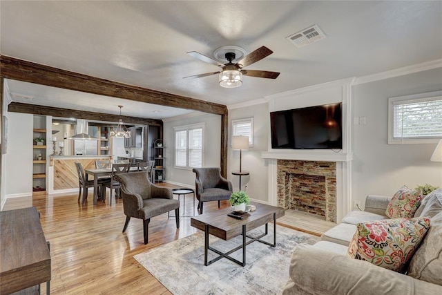 living room with ceiling fan with notable chandelier, ornamental molding, a fireplace, and light hardwood / wood-style flooring