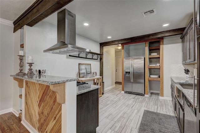 kitchen featuring light stone countertops, tasteful backsplash, stainless steel fridge with ice dispenser, island exhaust hood, and a breakfast bar