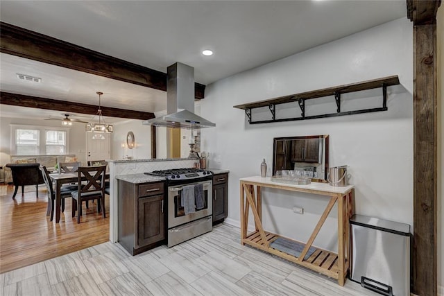 kitchen with dark brown cabinetry, ceiling fan, wall chimney exhaust hood, decorative light fixtures, and stainless steel range with gas stovetop