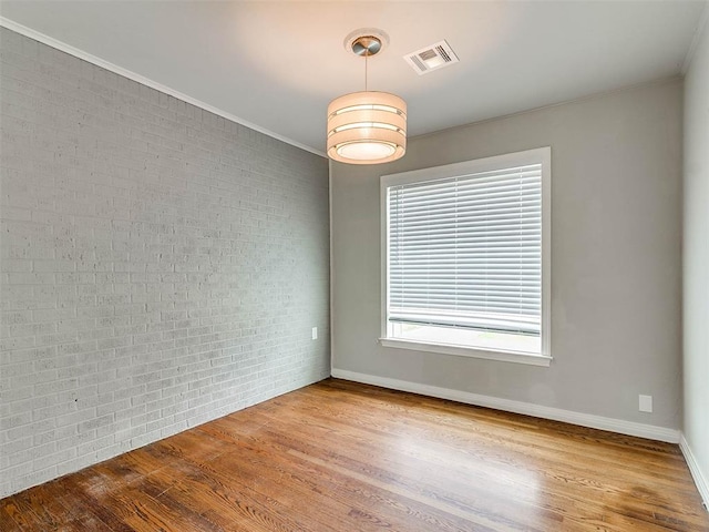 unfurnished room featuring light hardwood / wood-style floors, crown molding, and brick wall