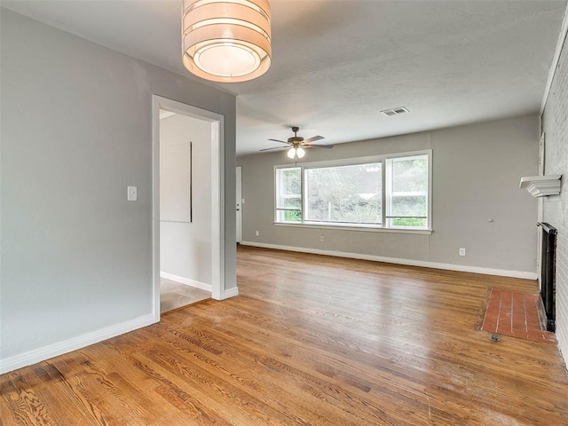 unfurnished living room with hardwood / wood-style flooring, a brick fireplace, and ceiling fan