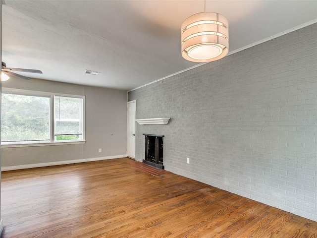 unfurnished living room featuring hardwood / wood-style floors, ceiling fan, a fireplace, and brick wall