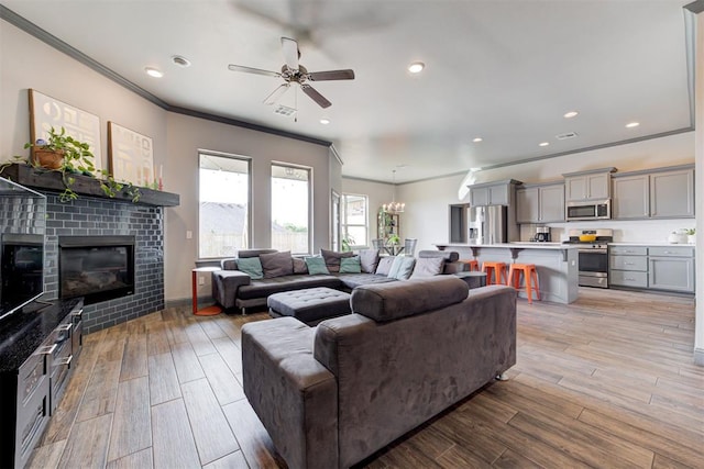 living room with a tile fireplace, ceiling fan with notable chandelier, light hardwood / wood-style floors, and ornamental molding