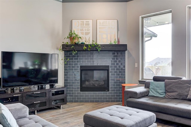 living room with light wood-type flooring, crown molding, and a brick fireplace