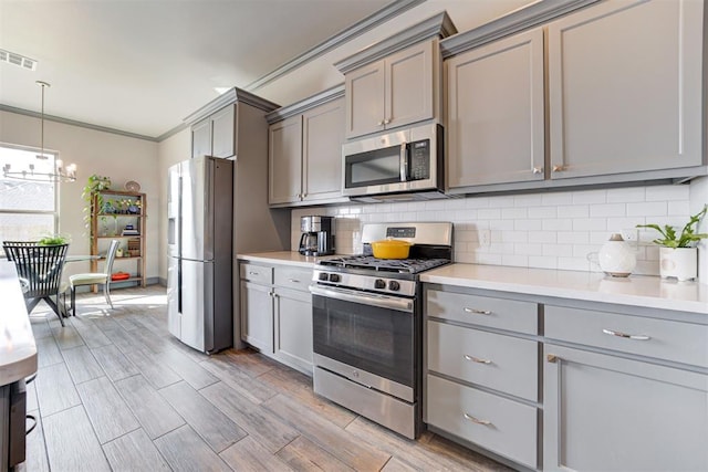 kitchen with stainless steel appliances, crown molding, gray cabinets, decorative backsplash, and light wood-type flooring