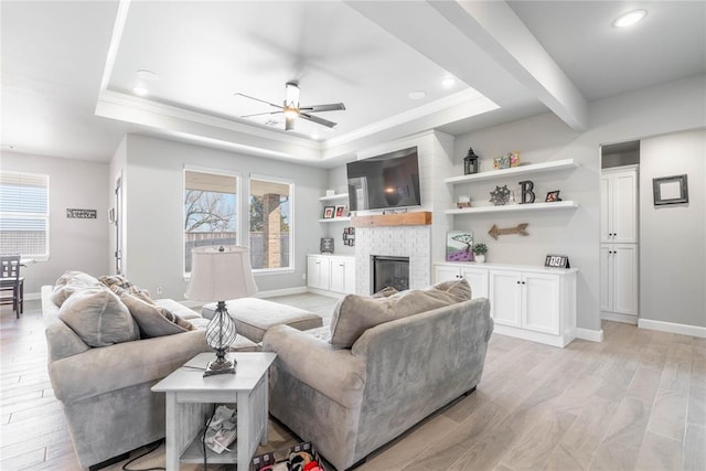 living room featuring a brick fireplace, a raised ceiling, light hardwood / wood-style flooring, and ceiling fan