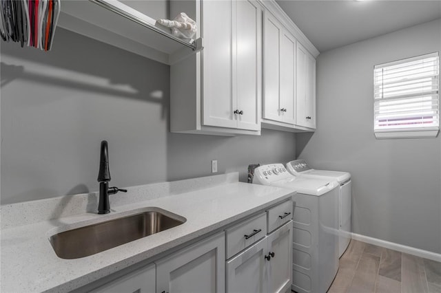 laundry area with washing machine and clothes dryer, sink, cabinets, and light wood-type flooring