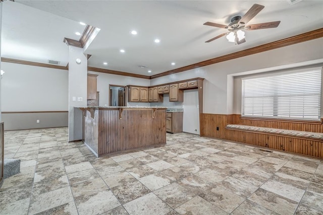 kitchen with kitchen peninsula, a breakfast bar, ceiling fan, wooden walls, and crown molding